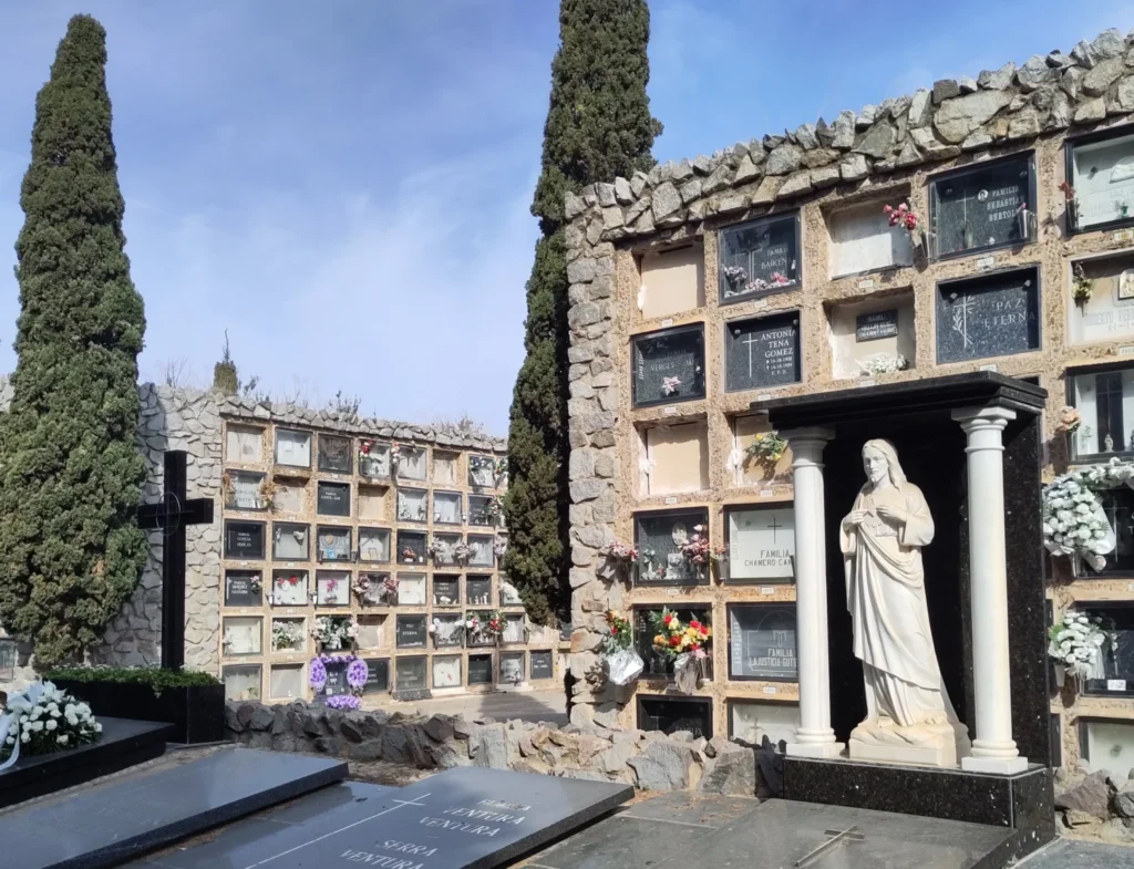 Gräber im Felsgartenfriedhof Cementiri Montjuïc in Barcelona. Vorne ein imposantes Grabmal mit Jesus zwischen zwei ionischen Säulen. 