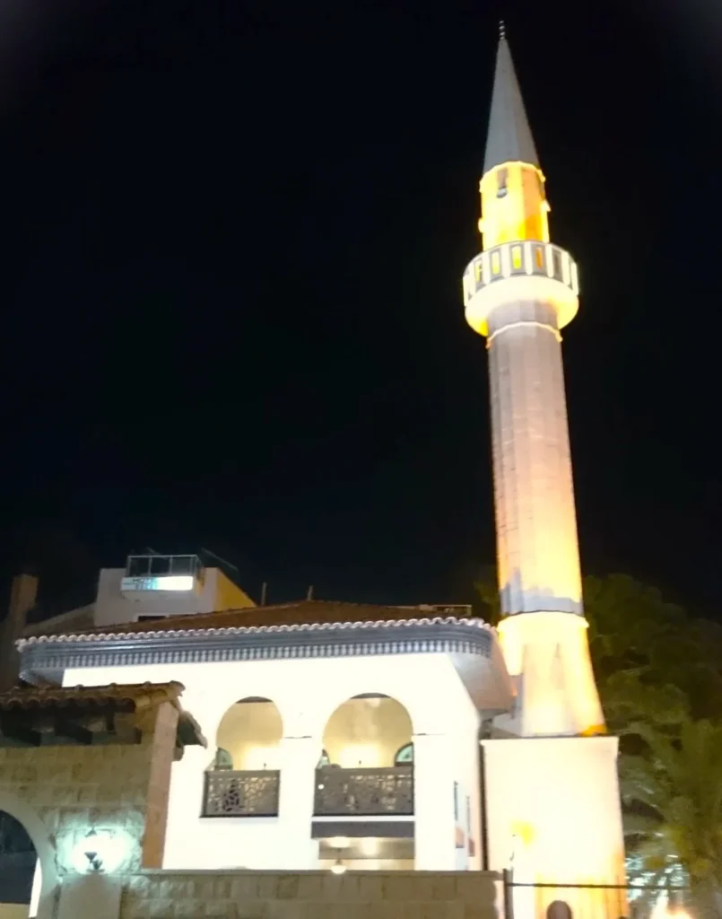 Beleuchtete, weiße Minarette einer Moschee in Ulcinj Montenegro bei Nacht. 