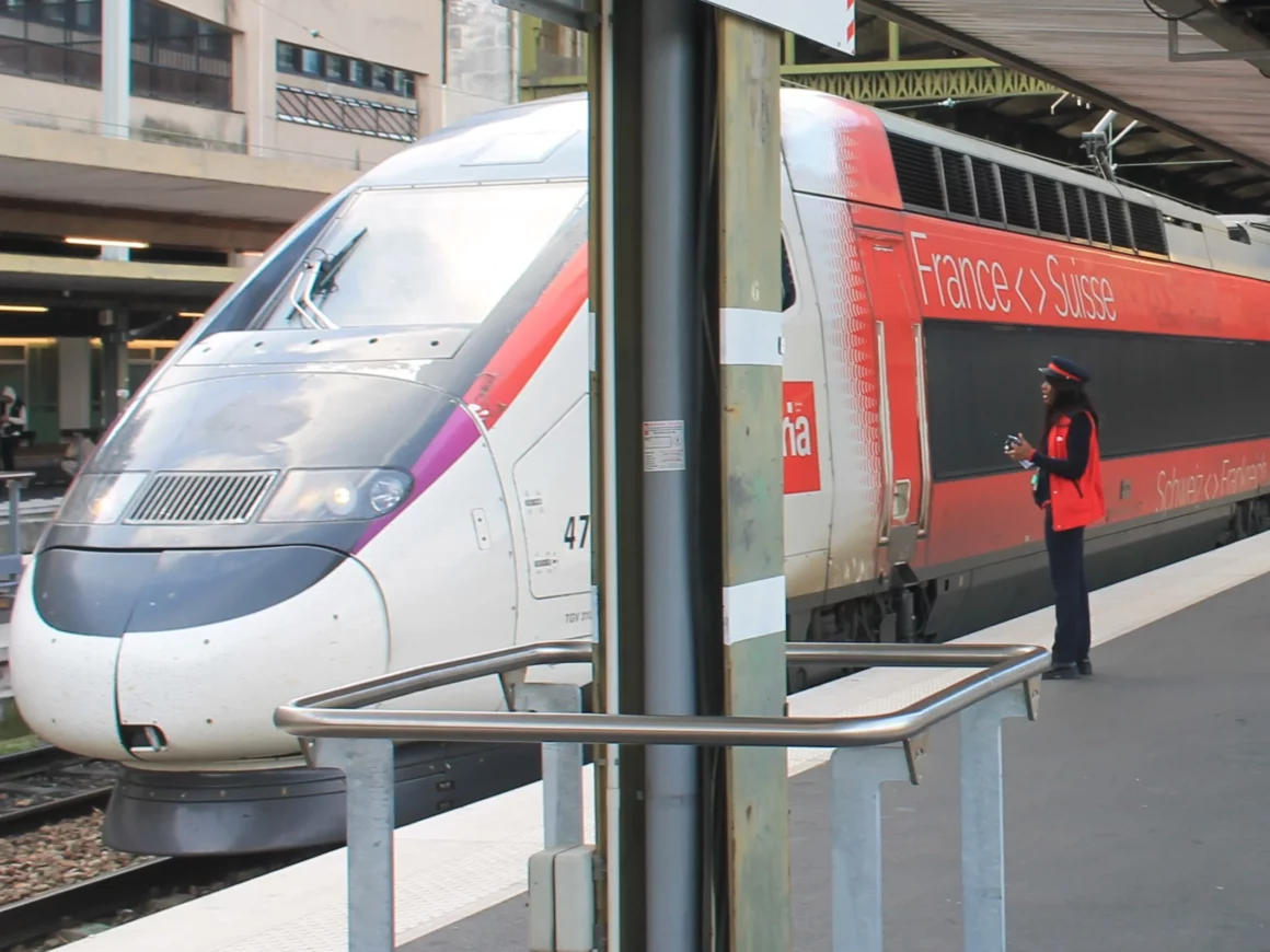 TGV Lyria auf dem Bahnsteig am Gare de Lyon in Paris. Neben dem Zug steht eine Schaffnerin, die mit der zugfuehrenden Person spricht.  