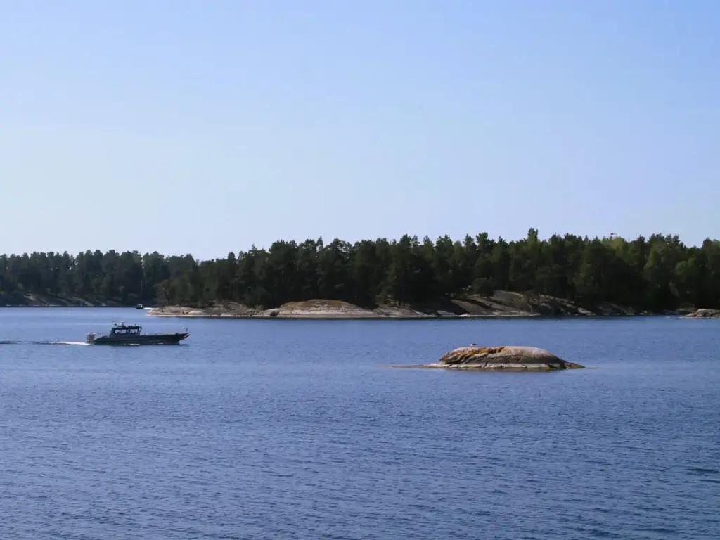 Mit Kiefern bewachsene Schäreninseln und ein Boot im blauen Wasser der Ostsee. 