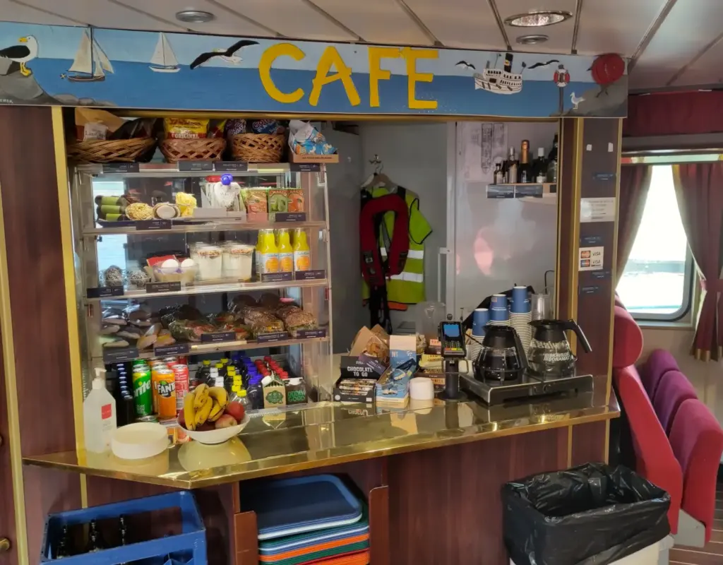 Kiosk im Innenraum der Fähre vom Waxholmsbolaget. Beschriftet mit "Cafe". Kannen mit Filterkaffee und Getränke, Snacks und Obst in der Auslage. 