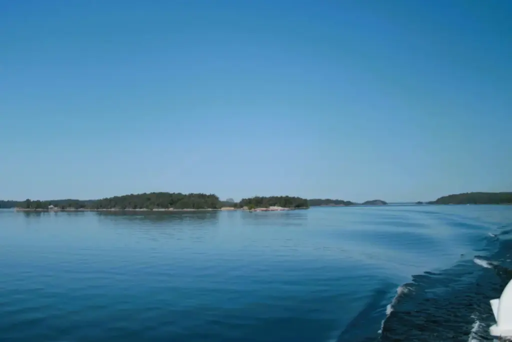 Kielwasser hinter der Fähre mit weitem Blick auf grüne Inseln in den Stockholm Schären. 