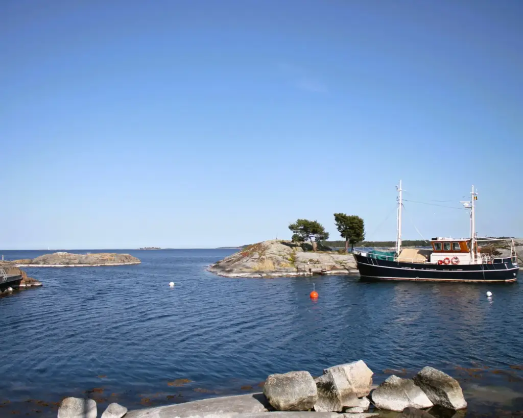 Blick auf offenen Stockholmer Schärengarten von Küste auf Möja aus.  Vor einem Felsen liegt ein kleines Segelboot. 