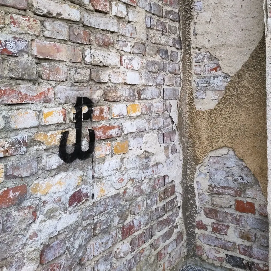 Offene Backsteinmauer mit abgetragenen Putz in Warschau. Steine in unterschiedlichen Farben in zufälliger Anordnung. Darauf ein Stencil der ehemaligen Widerstandsbewegung Kotwica (PW).