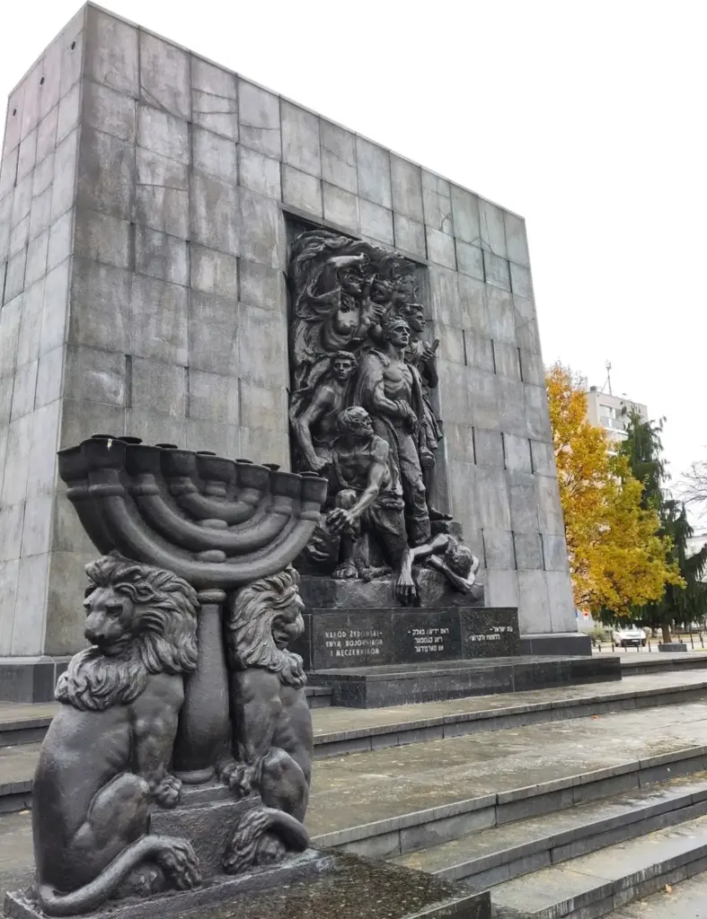 Warschauer Ghetto-Ehrenmal. Graue Stele mit heldenhaftem Bronzerelief. Davor die Skulptur eines iebenarmigen Leuchters