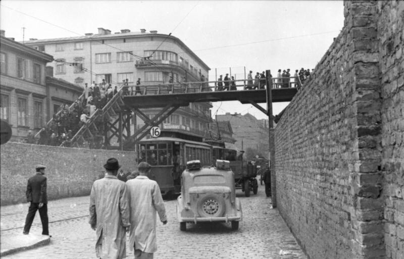 Schwarz-weißes Foto der Chlodna-Straße im Warschauer Ghetto mit Menschen auf der Brücke über den Mauern des Ghettos. 