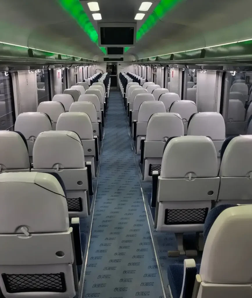 Leerer Sitzwagen im PKP Intercity mit modernen, grauen Sitzen, inklusive Klapptischen und Aufbewahrungsnetzen. Grüne Deckenbeleuchtung und Monitore.