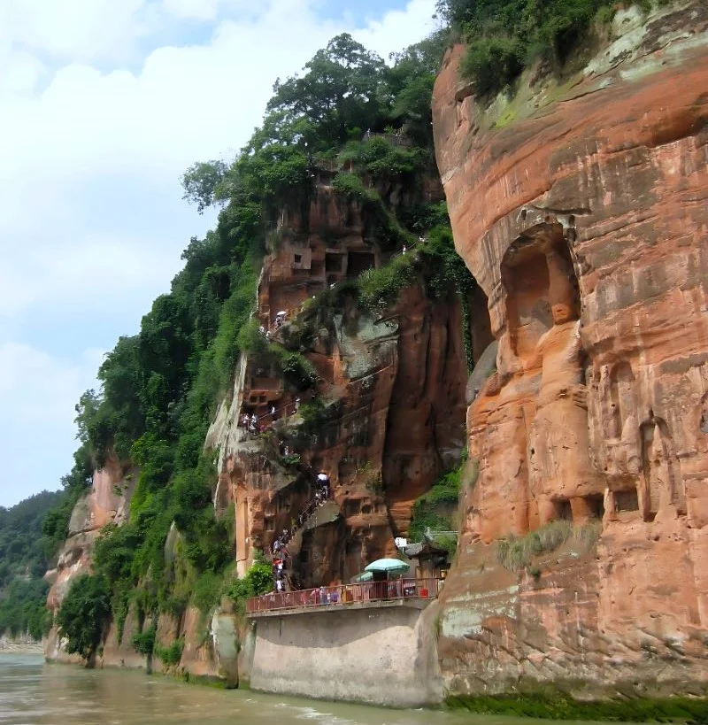 Roter Felsen mit eingemeißelten, buddhistischen Wächterfiguren. Treppen wie Ameisengänge im Fels für Touristinnen.