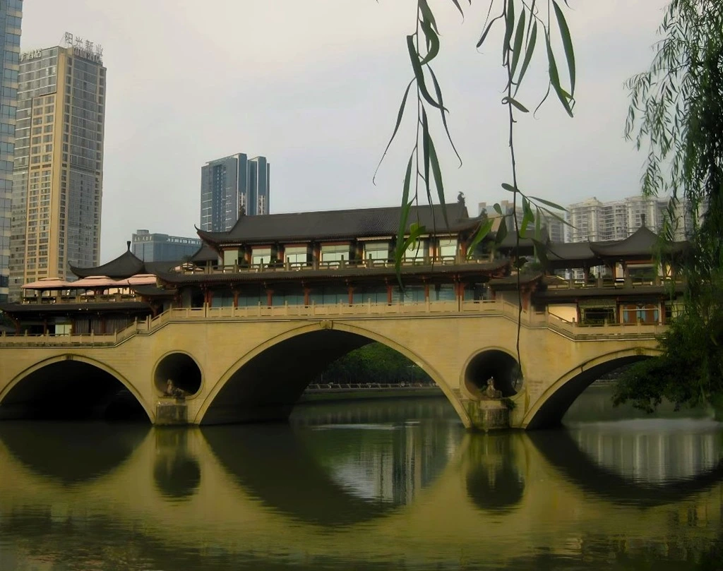 Die Anshun-Brücke in Chengdu spiegelt sich im Fluss. Im Hintergrund Hochhäuser. 