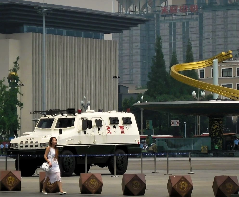 Eine Frau läuft vor einem gepanzerten Polizeiwagen, der auf dem Tianfu-Platz in Chengdu steht. Im Hintergrund eine der beiden Fontänen-Säulen. 