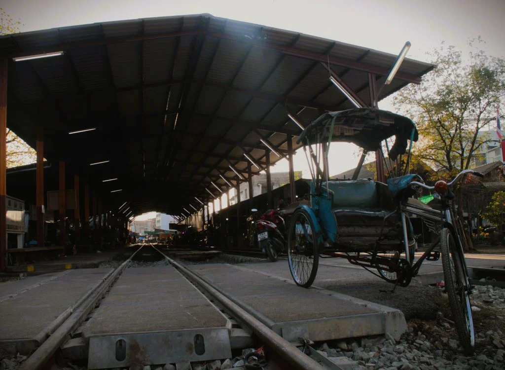 Verlassene Rikscha steht auf den Gleisen vor dem leeren Bahnhof Mae Klong. 