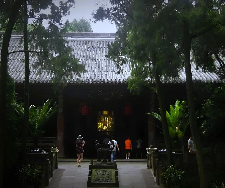 Eingang zum Wuhou Tempel in Chengdu. Kleine Allee mit grünen Bäumen. Am Ende Pavillon mit goldener Statue.