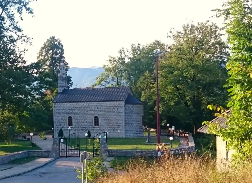 Kleine Steinkirche in Kolasin auf einer kleinen Grünfläche, umgeben von einigen Bäumen.