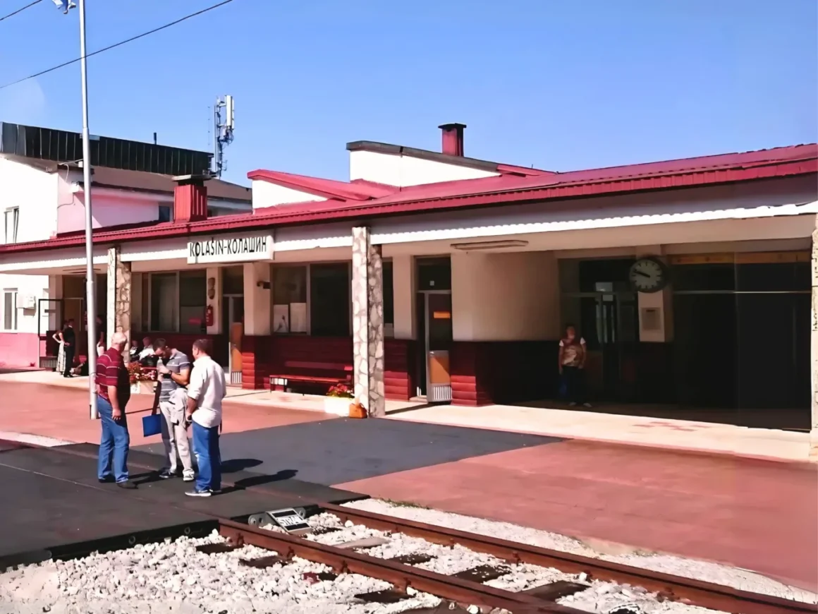 Bahnsteig und Empfangsgebäude des Bahnhofs von Kolasin. Drei Männer stehen auf dem Gleis. Einfaches Gebäude mit rotem Dach und roter Holzverkleidung.