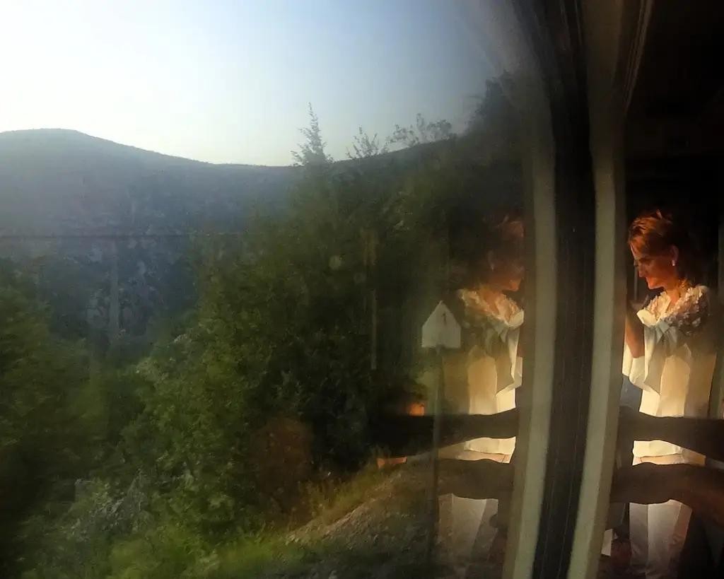 Blick aus dem Fenster des Tarazugs in Montenegro. Hinter dem Gebirge geht die Sonne unter. Eine Frau schaut aus dem Fenster.