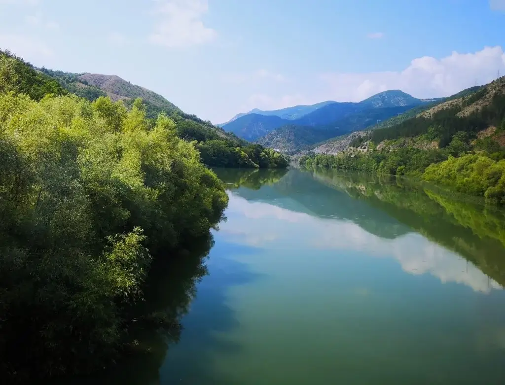 Blick über breiten Fluss in türkis und blau. Eingebettet in grünes Karstgebirge von Montenegro.
