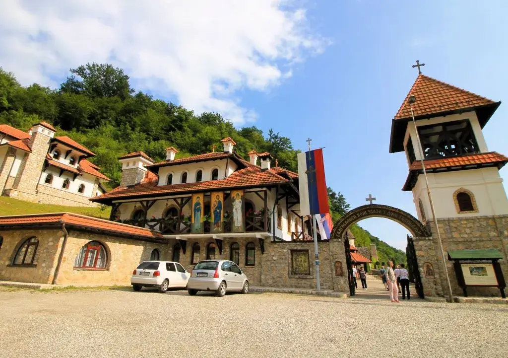 Eingang zum orthodoxen Kloster Kumanica in Vrbnica. Leute stehen unter Eingangsbogen mit Kreuz. Daneben ein kleiner Kirchturm.