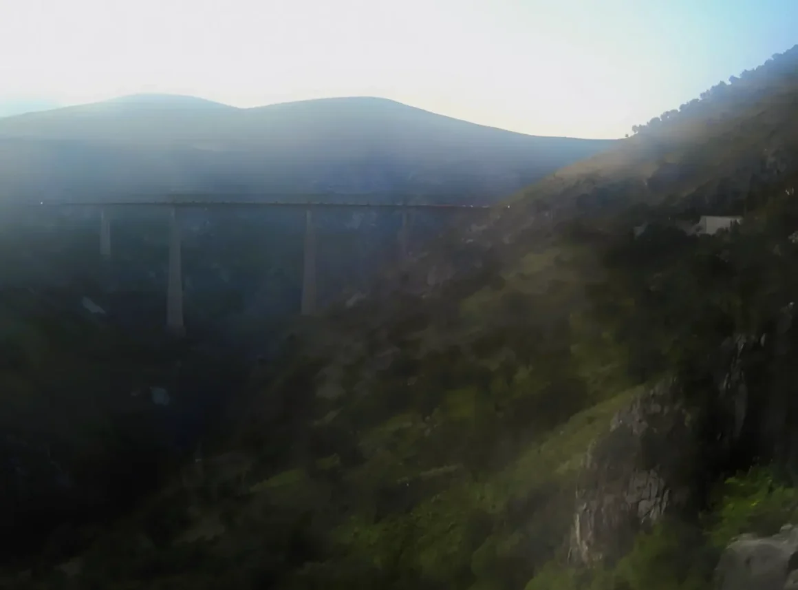 Die höchste Eisenbahnbrücke Europas vom Zug aus. Brücke überspannt breites Tal zwischen den Karstbergen. Gegenlicht der Sonne blendet.