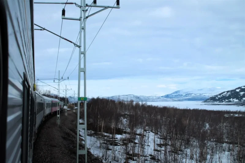 Arctic Circle Train - Blick in die verschneite Fjordlandschaft. Links der abbiegende Zug nach Narvik.