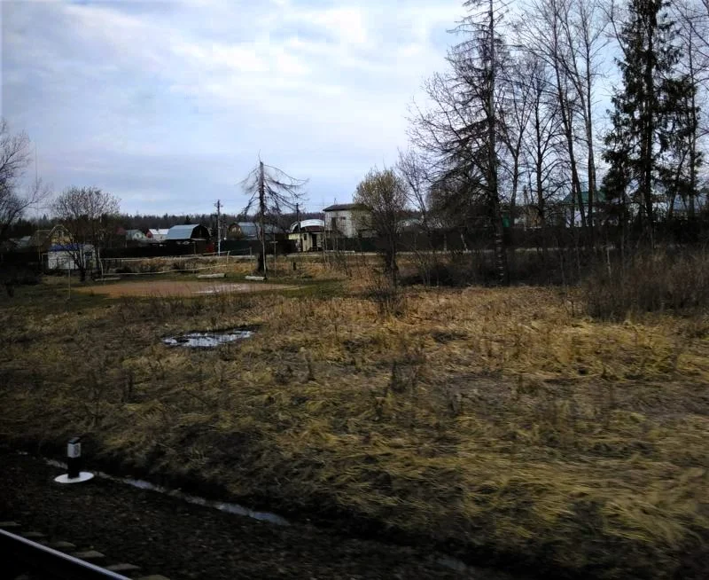 Neben den Schienen Feldrand und kahle Bäume. Dahinter ein kleines russisches Dorf, irgendwo vor Moskau.