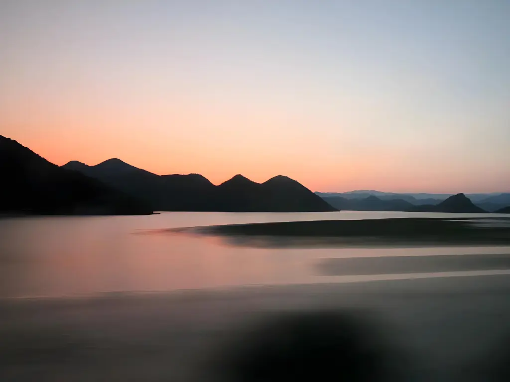 Silhouetten der Hügel am Skadarsee im Süden von Montenegro, nach dem Sonnenuntergang. Himmel orange, pink und blau.