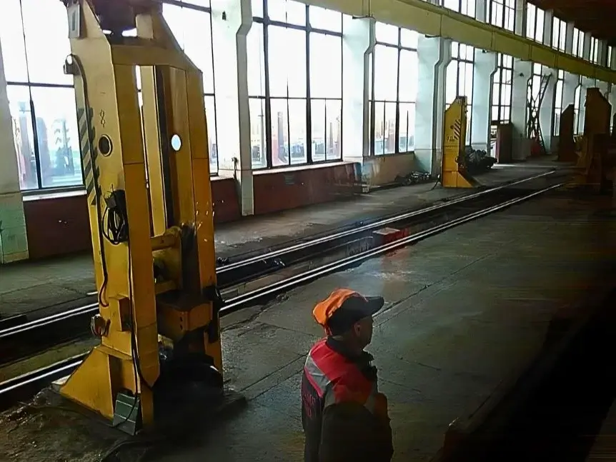 Umspurung am Bahnhof in Brest aus dem Zugfenster. Ein Arbeiter mit Mütze steht neben dem Schlafwagen. Daneben Schweres Gerät.