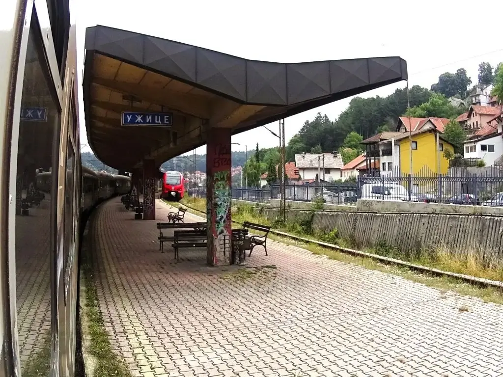 Zug am Bahnhof von Uzice. Schmaler Bahnsteig mit einfacher Überdachung und mehreren Sitzbänken.
