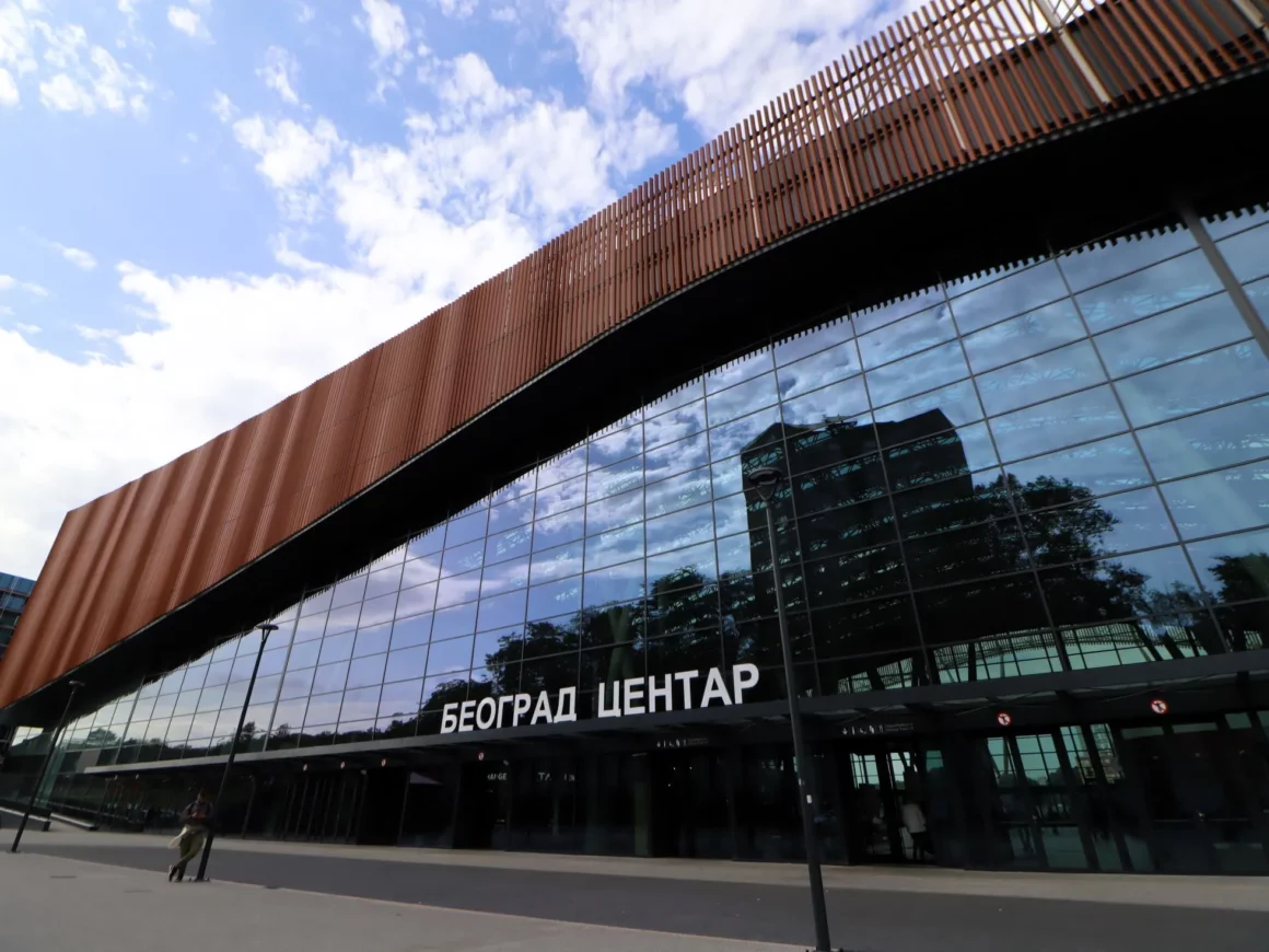 Haupteingang zum neuen Belgrader Hauptbahnhof "Beograd Centar". Moderne, spiegelnde Glasfassade mit einer Bogenförmigen Verkleidung aus rötlichen, senkrecht angeordneten Stangen am Dach.
