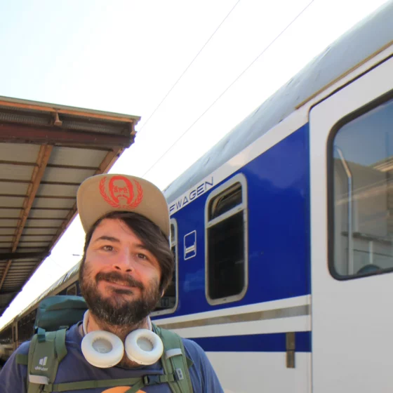 Meine Geschichte - Von kurzen Osteuropa Trips zu ausufernden East Rail Stories. Ich stehe mit Kopfhörern um den Hals vor einem blau-weißen Schlafwagen am Bahnsteig.