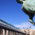 Pariser Metro fährt auf einer Trasse über die Bir Hakeim Brücke. Davor das Hinterteil einer bronzenen Pferdestatue.