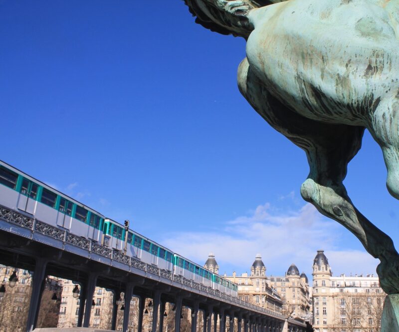 Pariser Metro fährt auf einer Trasse über die Bir Hakeim Brücke. Davor das Hinterteil einer bronzenen Pferdestatue.