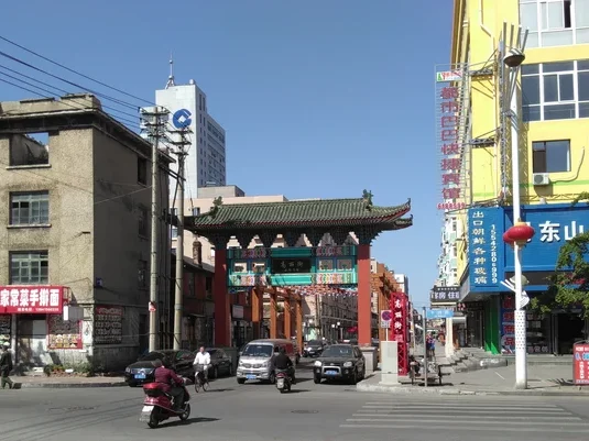 Straßenaufnahme des Eingangs zur Koryo Street in Dandong. Autos fahren durch ein traditionelles chinesisches Tor. 