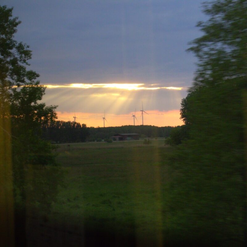 Orangefarbene Sonnenstrahlen durchbrechen Wolkendecke über der Landschaft.