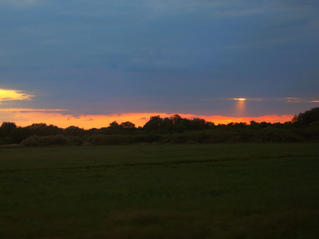 Roter Sonnenuntergang unter dichter Wolkendecke aus dem Zugfenster. 